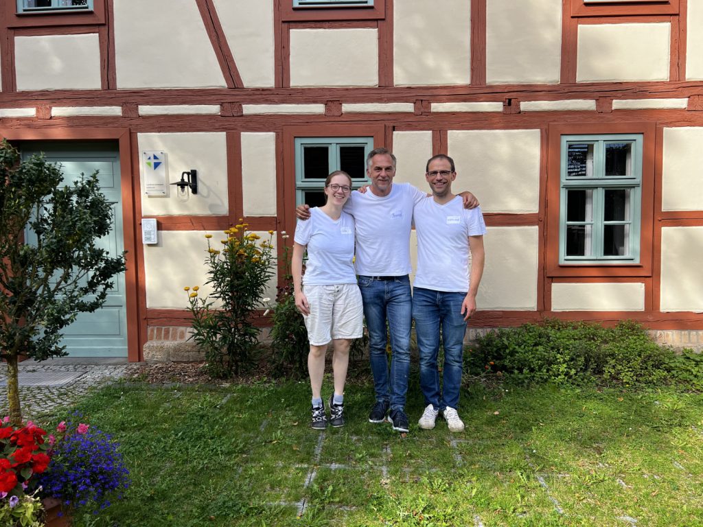 Die drei Vorstandsmitglieder Julia, Bernd und Nikolaus stehen im Schulterschluss vor einem Fachwerkhaus.